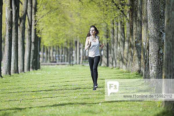 Confident young woman looking away while running on grassy land in park
