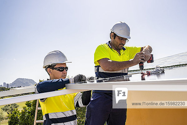 Männliche Techniker bei der Installation von Sonnenkollektoren auf dem Hausdach gegen den Himmel an einem sonnigen Tag