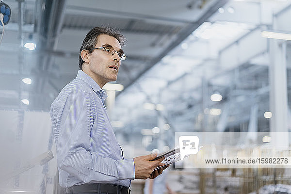 Mature businessman with documents and tablet in a factory