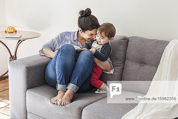 Glückliche Mutter sitzt auf der Couch und kuschelt mit ihrem kleinen Sohn