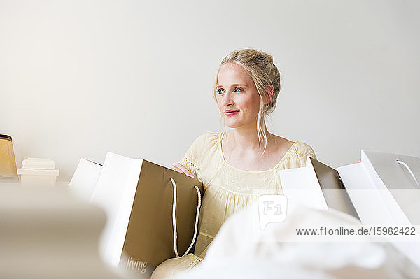 Portrait of happy blond woman sitting on bed between shopping bags