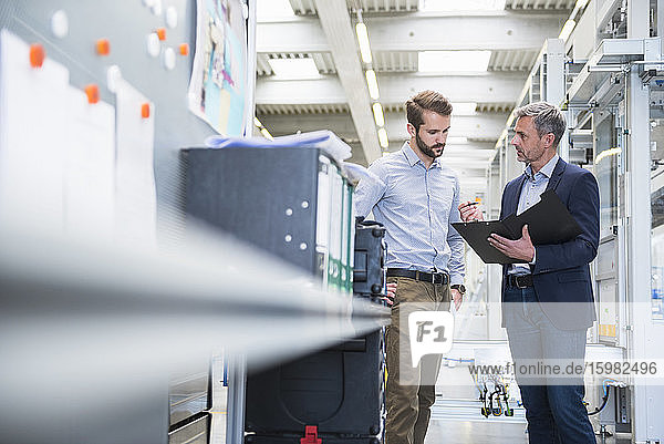 Two businessmen with folder talking in a factory