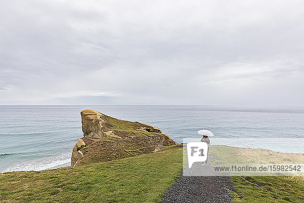 Neuseeland  Ozeanien  Südinsel  Otago  Dunedin  Rückansicht einer Frau mit Regenschirm auf einem Fußweg in der Nähe von Tunnel Beach