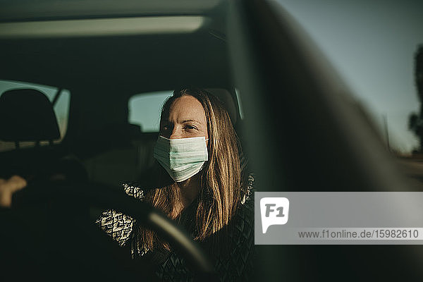 Mittlere erwachsene Frau mit Schutzmaske im Auto