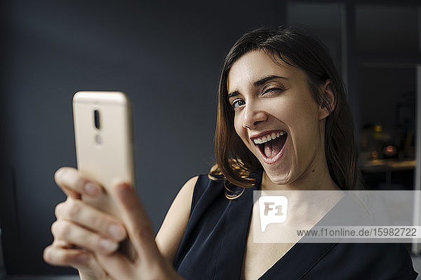 Porträt einer jungen Frau mit Smartphone  die lustige Gesichter zieht