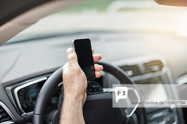 Cropped hand of man holding smart phone over steering wheel in car