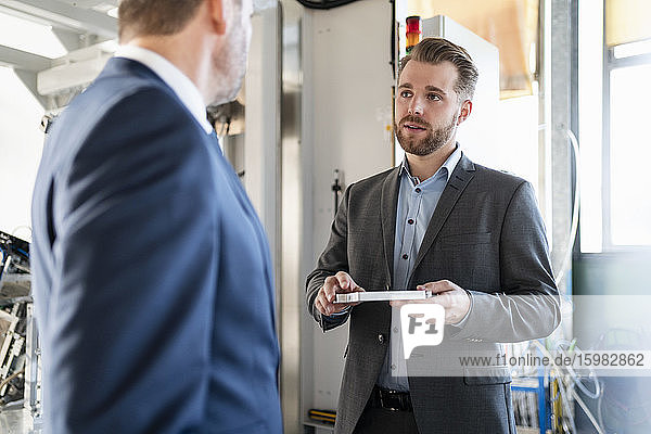 Two businessmen having a meeting in a factory discussing workpiece