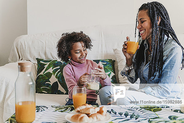 Happy mother and her little daughter drinking smoothie and juice at home