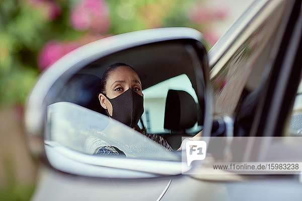 Frau mit Gesichtsmaske fährt Auto  das im Spiegel reflektiert wird
