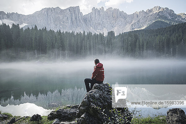 Schweiz  Junger Mann sitzt im Morgengrauen am Lago di Carezza in den Dolomiten