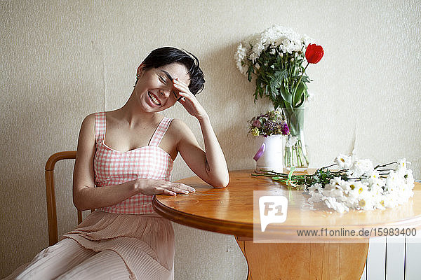 Junge Frau sitzt mit Blumen am Tisch