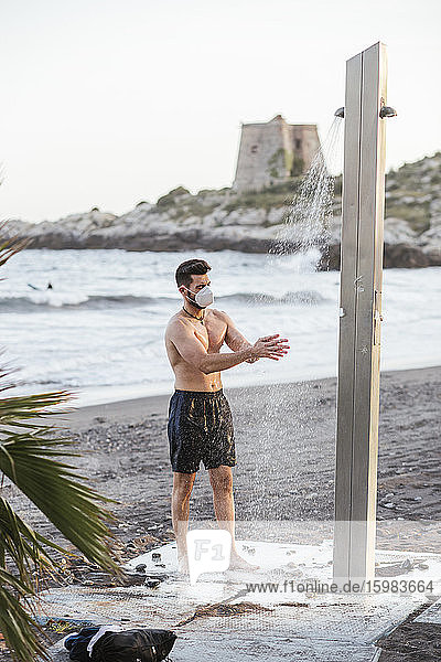 Shirtless Mitte erwachsenen Mann Waschen der Hände unter der Dusche am Strand gegen klaren Himmel bei Sonnenuntergang