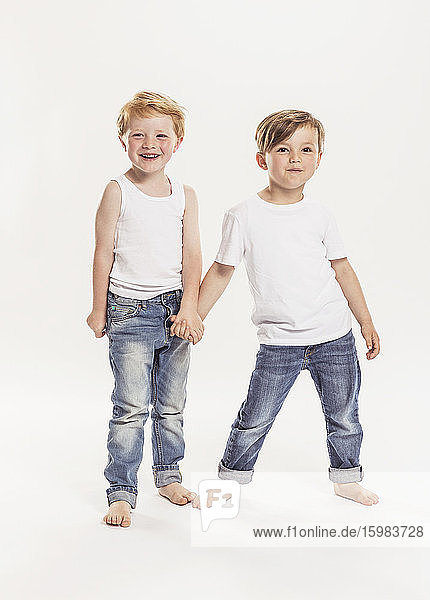 Portrait of two little boys holding hands in front of white background