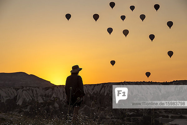 Rückansicht einer jungen Frau mit Silhouette  die Heißluftballons betrachtet  während sie an Land in Goreme  Kappadokien  Türkei steht