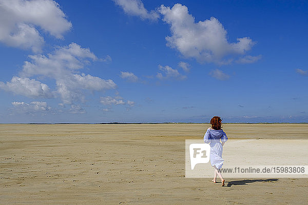 Full length rear view of teenage girl walking on sand at beach during sunny day