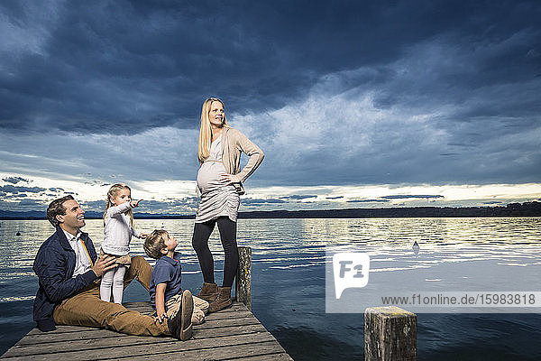 Glückliche Familie in voller Länge auf dem Steg am Starnberger See vor bewölktem Himmel