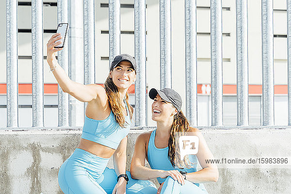 Junge Frau nimmt Selfie mit Zwillingsschwester gegen Zaun von Smart Phone