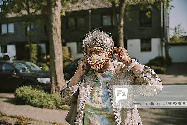 Frau im Ruhestand trägt einen Gesichtsschutz  während sie an einem sonnigen Tag im Freien steht
