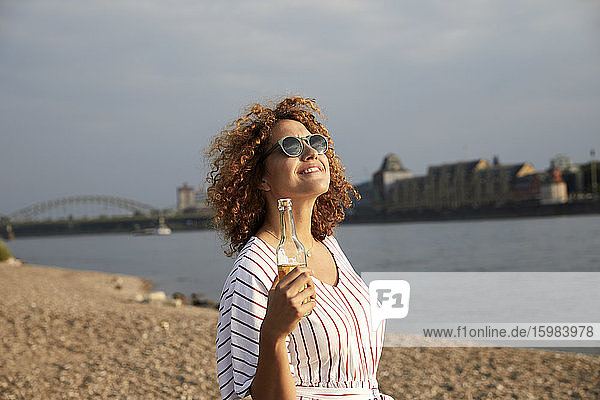 Portrait of smiling woman with glass bottle at riverside