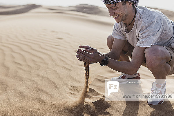 Glücklicher männlicher Tourist spielt mit Sand in der Wüste in Dubai  Vereinigte Arabische Emirate