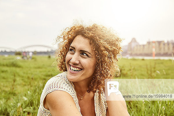 Porträt einer lächelnden Frau  die auf einer Wiese sitzt und zur Seite schaut
