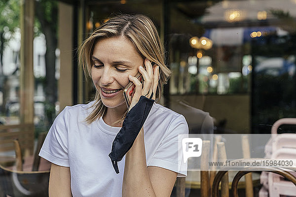 Portrait of smiling woman on the phone with protective mask in her hand in front of a closed coffee shop
