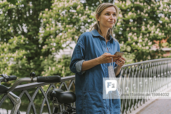 Frau auf einer Brücke mit Gesichtsmaske  Smartphone und Fahrrad