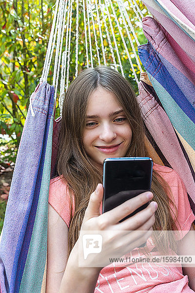 Portrait of smiling girl in hammock looking at cell phone
