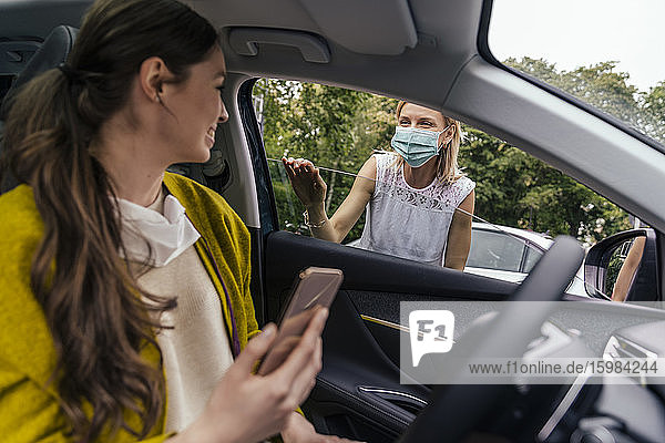 Woman wearing a protective mask talking through car window with woman without mask
