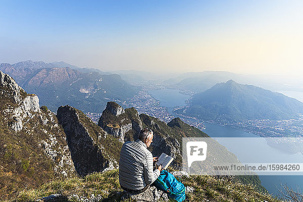 Rear view of hiker reading a book on mountaintop  Orobie Alps  Lecco  Italy