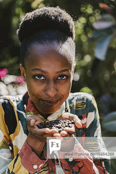 Porträt einer lächelnden jungen Frau  die geröstete Kaffeebohnen in den Händen hält