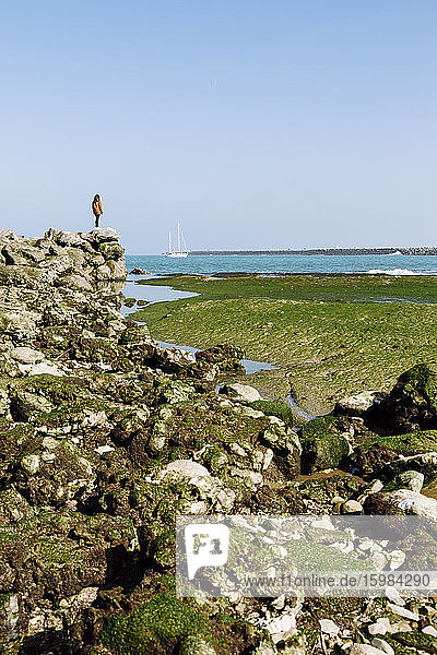 Frau  die am Rande einer Felsformation am Strand gegen den klaren blauen Himmel an einem sonnigen Tag steht