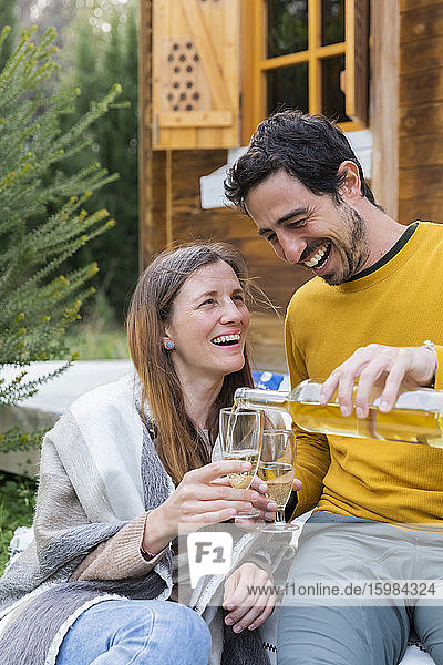 Happy man pouring wine in glass held by girlfriend while sitting outdoors