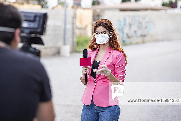 Mann filmt Reporter mit Maske  während er auf der Straße steht