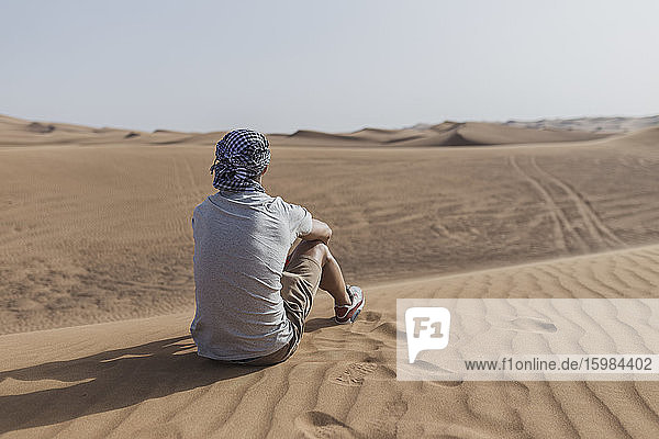 Männlicher Tourist sitzt auf Sanddünen in der Wüste von Dubai  Vereinigte Arabische Emirate