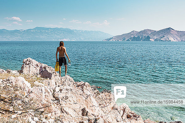 Kroatien  Krk  Mann steht auf einer Felsformation und schaut aufs Meer