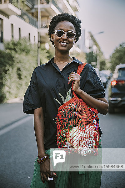 Porträt einer lächelnden jungen Frau  die mit ihrem Einkauf auf der Straße steht