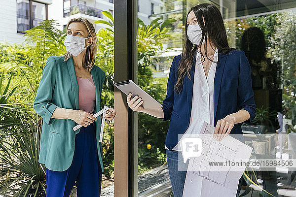 Zwei Immobilienmakler mit Gesichtsmasken bei der Inspektion des Außenbereichs eines Hauses