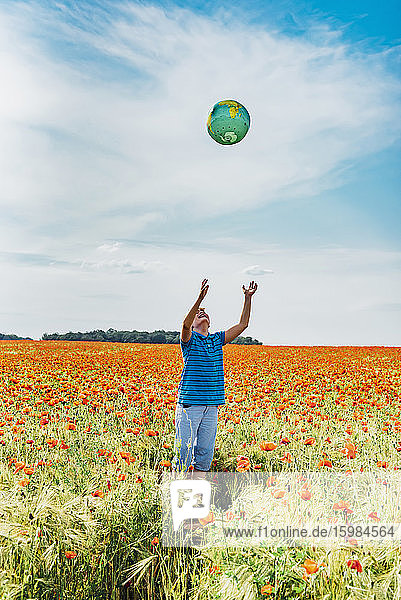 Boy catching globe while standing in poppy field against sky