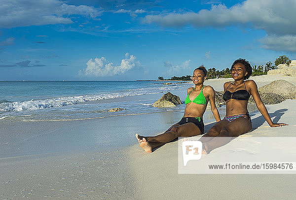 Lächelnde Freundinnen in Bikinis entspannen sich am Strand von Grace Bay bei Sonnenuntergang  Providenciales  Turks- und Caicosinseln