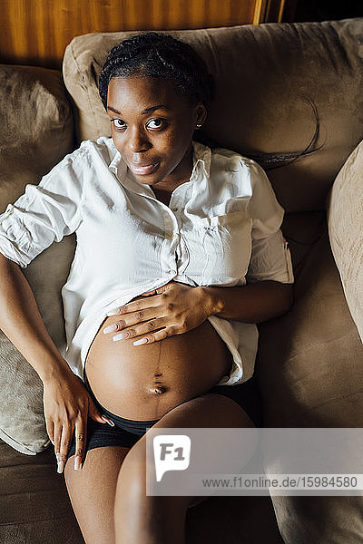 Porträt einer schwangeren jungen Frau auf der Couch