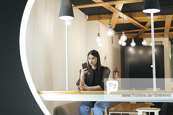 Selbstbewusste junge Frau  die in einem Café sitzt und ihr Smartphone benutzt
