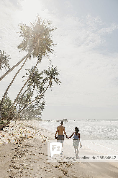 Paar in voller Länge am Strand spazierend gegen den Himmel an einem sonnigen Tag  Sri Lanka