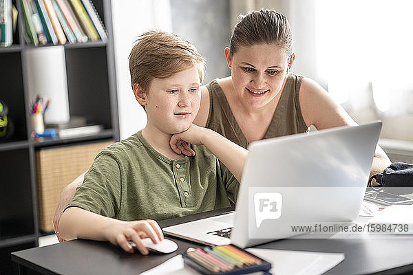 Mother homeschooling her son and using laptop at home