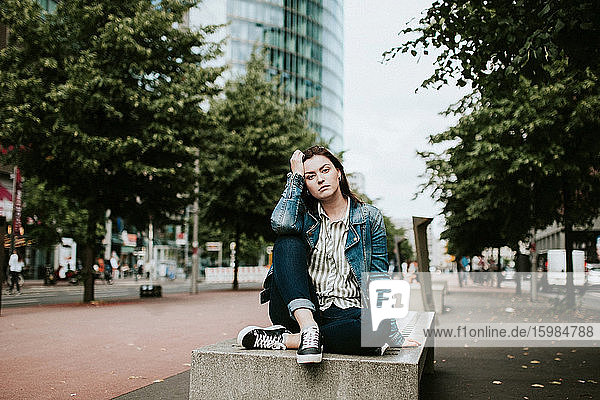 Deutschland  Berlin  Porträt einer im Freien sitzenden jungen Frau mit der Hand im Haar