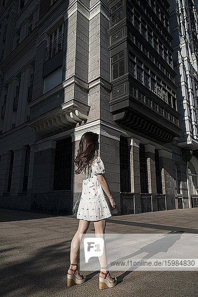 Junge Frau in weißem Minikleid steht auf einer Straße in der Stadt an einem sonnigen Tag