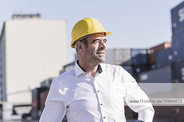 Porträt eines Geschäftsmannes mit Schutzhelm auf einem Industriegelände mit Blick in die Ferne