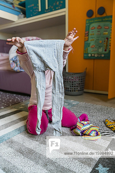 Preschool girl holding leggings while kneeling on carpet in bedroom at home