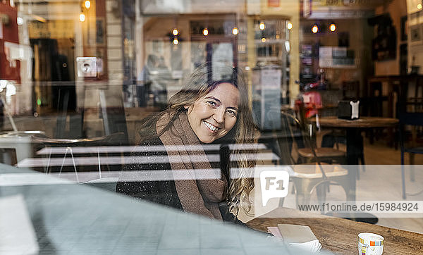 Lächelnde Frau  die durch die Fensterscheibe eines Cafés schaut
