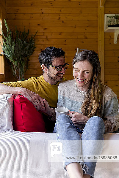 Fröhliches Paar hält sich an den Händen und entspannt sich auf dem Sofa in einer Blockhütte